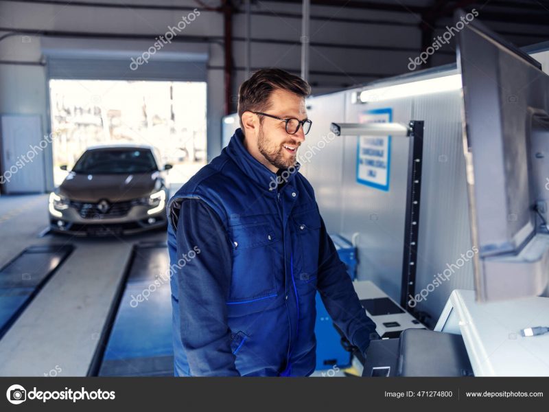 Technical inspection of the car. Car diagnostics on technical inspection, car electronics. A man in a blue uniform stands in front of the computer and adjusts the screen view parameters